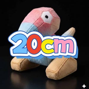 May include: A soft toy in the shape of a geometric figure, with pink, blue, and white panels. The toy has a large eye and tan feet. The text "20cm" is displayed in a blue, red, yellow, and pink bubble.