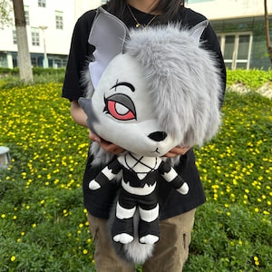 May include: A gray and white plush toy with black and white stripes. The toy has a long, fluffy tail and a face with red eyes and a black nose.