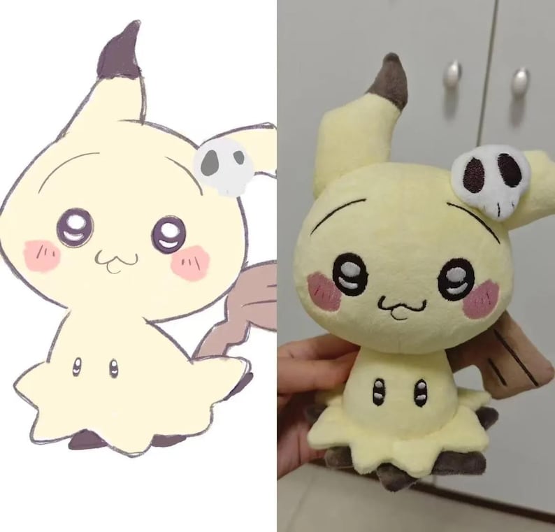 May include: A light yellow Mimikyu plush toy, featuring a black and white skull-shaped accessory. The toy has large black eyes, pink cheeks, and a small, smiling mouth. The design is based on the popular Pok&eacute;mon character.