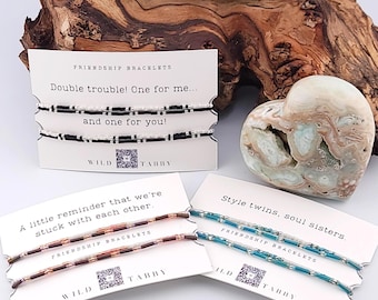 Può includere: Braccialetti dell'amicizia con il testo "Double trouble! One for me... and one for you!" e "A little reminder that we're stuck with each other." e "Style twins, soul sisters." I braccialetti sono neri, marroni e verde acqua.