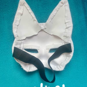 May include: A white animal-shaped mask featuring pointed ears and a smooth, rigid surface. The back of the mask is lined with white fabric trim along the edges and includes a black elastic strap for securing it. The word unlined is printed below.