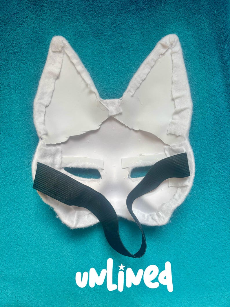 May include: A white animal-shaped mask featuring pointed ears and a smooth, rigid surface. The back of the mask is lined with white fabric trim along the edges and includes a black elastic strap for securing it. The word unlined is printed below.