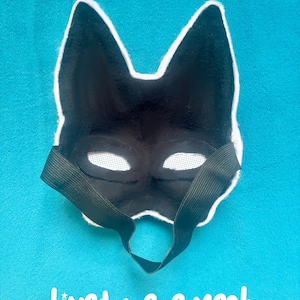 May include: A black animal-shaped mask with pointed ears and white mesh over the eye openings. The interior of the mask is lined with black fabric and features a black elastic strap for securing it. The text Lined + eye mesh is visible.