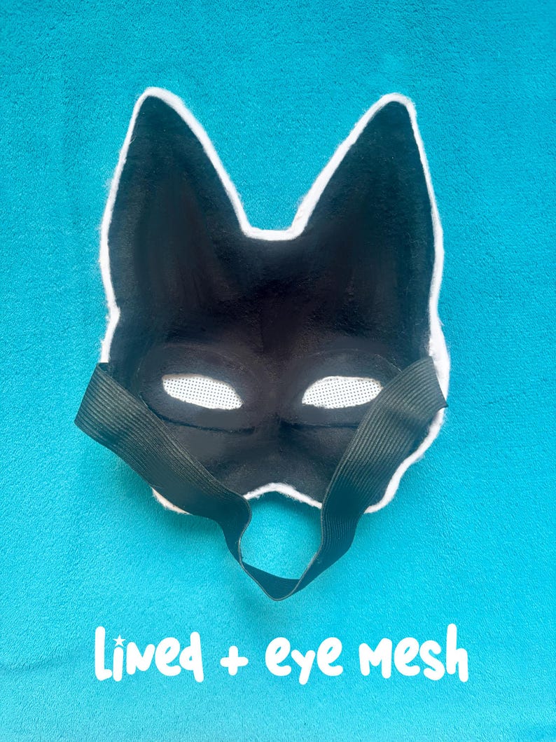 May include: A black animal-shaped mask with pointed ears and white mesh over the eye openings. The interior of the mask is lined with black fabric and features a black elastic strap for securing it. The text Lined + eye mesh is visible.