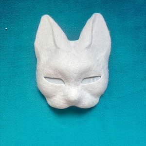 May include: A white, textured animal mask featuring pointed ears and narrow, mesh-covered eye openings. The mask has a molded, rounded snout area and a smooth, felt-like surface texture, designed to cover the upper portion of the face.