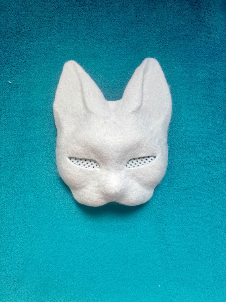 May include: A white, textured animal mask featuring pointed ears and narrow, mesh-covered eye openings. The mask has a molded, rounded snout area and a smooth, felt-like surface texture, designed to cover the upper portion of the face.