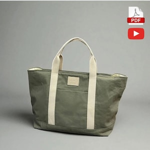 May include: An olive green tote bag with cream-coloured handles and accents. The bag has a front pocket and a small rectangular patch with a logo. The bag is made of a durable material and is designed for everyday use.
