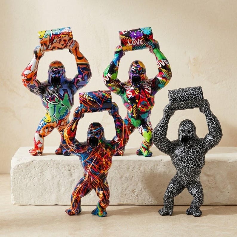 May include: Four gorilla figurines standing in a row, each holding a rectangular block above its head. The figures feature various colorful graffiti patterns, including bright orange, green, blue, and black designs, with one figure in a black and white crackle pattern.