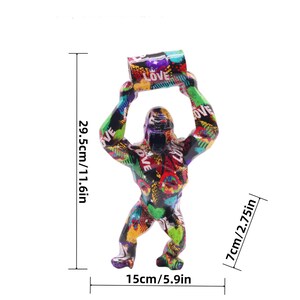 May include: A gorilla figurine featuring a vibrant graffiti-style pattern with the word LOVE printed repeatedly. The figure measures 11.6 inches in height, 5.9 inches in width, and 2.75 inches in depth, shown with visible dimension lines.