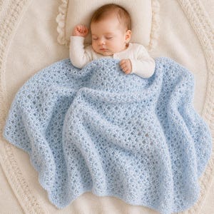 May include: A sleeping baby is nestled under a light blue, open-weave crochet blanket. The blanket has a scalloped edge and covers the baby, who is wearing a white long-sleeved shirt. The baby rests on a cream-colored pillow and blanket.