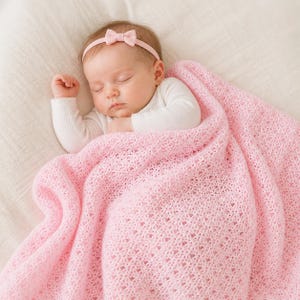 May include: A sleeping baby wrapped in a soft, pink, open-weave blanket. The baby wears a white long-sleeved onesie and a pink headband with a bow. The blanket is draped over the baby, creating a cozy and comforting scene.