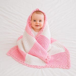 Peut inclure: Une couverture pour bébé crochetée à la main avec un motif carré alternant des blocs de laine rose tendre et blanche. La couverture présente une bordure festonnée décorative et est drapée sur la tête et les épaules d'un nourrisson souriant.