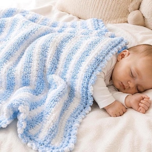 May include: A crocheted baby blanket featuring alternating vertical stripes of light blue and white yarn. The blanket has a textured, raised stitch pattern and a scalloped edge, draped over a sleeping infant wearing a white long-sleeve shirt.