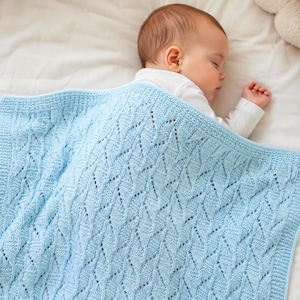 Peut inclure: Un bébé dort sous une couverture tricotée bleu clair. La couverture présente un motif ajouré détaillé et une bordure unie. Le bébé porte un body blanc. La couverture mesure environ 91 cm sur 91 cm.