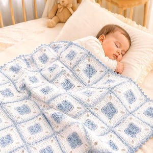 May include: A sleeping baby is covered by a handmade, white and pale blue crochet blanket. The blanket has a square pattern with floral designs and a scalloped edge. The baby wears a white onesie.