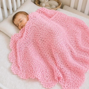 May include: A soft, light pink baby blanket featuring an intricate, open-work crochet pattern with a delicate scalloped edge. The blanket is draped over a sleeping infant, showcasing the detailed texture of the yarn and the decorative border.