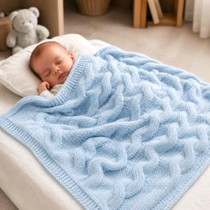 May include: A light blue knitted baby blanket featuring a prominent cable knit pattern with wavy vertical columns. The blanket is rectangular with a ribbed border and is draped over a sleeping infant resting on a white pillow.