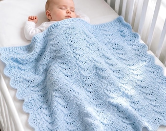 May include: A sleeping baby is nestled in a white crib, covered by a light blue, scalloped-edge knitted blanket. The blanket has a delicate, openwork design. The baby is wearing a white long-sleeved onesie.