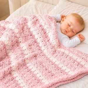 May include: A sleeping baby is nestled under a soft, pink and white crocheted blanket. The blanket features a textured pattern with alternating rows of pink and white. The baby is wearing a white long-sleeved onesie.
