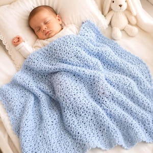 May include: A sleeping baby is nestled under a light blue crocheted blanket. The blanket has a delicate, open weave pattern. A white stuffed bunny sits nearby on the bed. The baby is wearing a white onesie.
