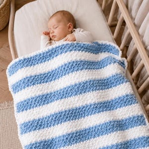 May include: A sleeping baby in a crib, covered with a blue and white striped blanket. The blanket has a textured, raised pattern. The crib is made of light-colored wood.