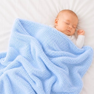 May include: A sleeping baby wrapped in a soft, light blue blanket. The baby is wearing a white onesie and is resting on a white sheet. The blanket has a textured, plush appearance.