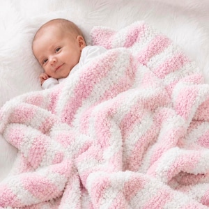 May include: A baby wrapped in a soft, textured blanket featuring alternating diagonal stripes of light pink and white. The blanket has a plush, fuzzy appearance with a consistent knit pattern throughout, providing a cozy layer over the infant.