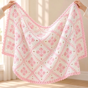 Könnte beinhalten: Eine quadratische Häkeldecke mit einem sich wiederholenden Muster aus weißen und hellrosa Blumenmotiven, die in Rautenform angeordnet sind. Die Decke ist an allen vier Kanten mit einer hellrosa, bogenförmigen Bordüre versehen.