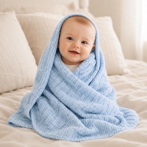 May include: A baby wrapped in a light blue knitted blanket with a ribbed texture. The blanket covers the baby's head and shoulders, draping down in soft folds. The knit fabric features a consistent vertical pattern throughout the entire piece.