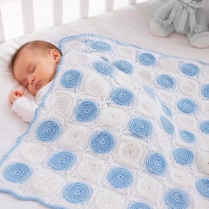 May include: A handmade crochet baby blanket featuring a repeating pattern of alternating white and light blue circular motifs arranged in square blocks. The blanket has a scalloped light blue border and is draped over a sleeping infant.