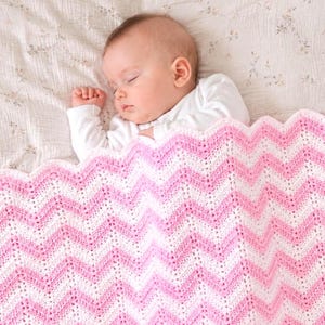 Könnte beinhalten: Ein schlafendes Baby liegt unter einer rosa-weiß karierten Decke. Die Decke hat einen gewellten Rand. Das Baby trägt einen weißen Langarm-Body. Der Hintergrund ist ein Bettlaken mit Blumenmuster.