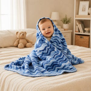 May include: A soft, knitted baby blanket featuring a wavy chevron pattern in various shades of blue, including navy, royal, and light blue. The blanket is draped over a smiling infant, covering their head and shoulders, with a brown teddy bear nearby.