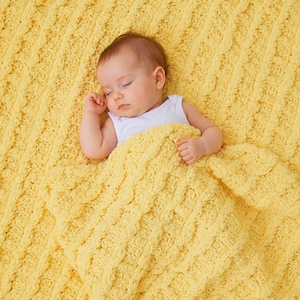 May include: A bright yellow knitted blanket featuring a textured cable knit pattern. The blanket has a soft, chunky yarn construction with vertical rows of braided stitches, providing a thick and cozy appearance across the entire surface.