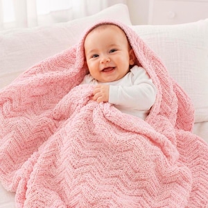 May include: A smiling baby wrapped in a soft, pink knitted blanket with a chevron pattern. The baby is wearing a white long-sleeved shirt. The blanket is draped over the baby's head, creating a cozy and comforting scene.