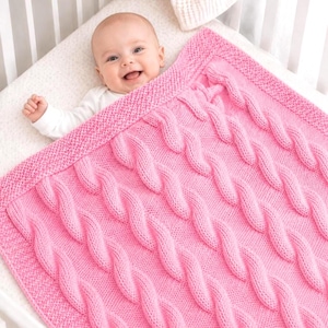 May include: A bright pink knitted baby blanket featuring a prominent cable knit pattern throughout the center and a textured seed stitch border. The blanket is rectangular in shape and displays a consistent, uniform yarn color and stitch density.