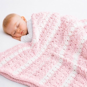 May include: A sleeping baby is nestled under a soft, pink and white crocheted blanket. The blanket features a textured pattern and provides a cozy and comforting environment. The baby is wearing a white long-sleeved shirt.