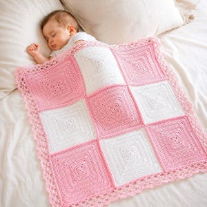 May include: A square crochet baby blanket featuring a checkerboard pattern of alternating pink and white squares. The blanket is finished with a decorative scalloped crochet border along all four edges, creating a textured and detailed design.