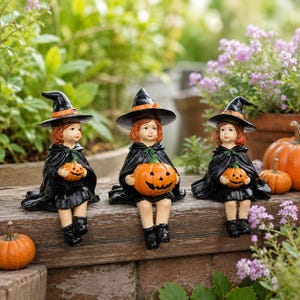 May include: Three figurines of children dressed as witches, each wearing a black pointed hat with an orange band and a black cape. Each figure has reddish-brown hair and holds a small orange jack-o'-lantern pumpkin in their hands.