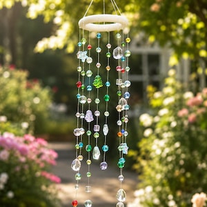 May include: A hanging mobile featuring a white circular frame with multiple thin strings suspended from it. Each string is adorned with various multi-colored glass beads in shapes including stars, trees, spheres, and faceted crystals.