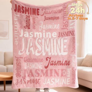 May include: A pink blanket featuring the name "Jasmine" in a repeating pattern of red and white fonts. The blanket is displayed, with the text "Ships in 24h" and "Arrives in 5-7 days" visible.