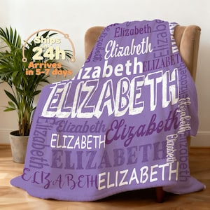Pode incluir: Um cobertor lavanda com o nome "Elizabeth" em várias fontes e tamanhos. A palavra "Elizabeth" é repetida no cobertor em branco e roxo. O cobertor está sobre uma poltrona bege.