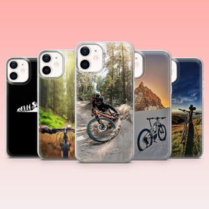 May include: A selection of phone cases showcasing outdoor themes. Designs include a mountain biker, a mountain landscape, a forest trail, and a bicycle silhouette. The cases are in clear protective covers.