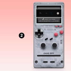 May include: A clear phone case with a retro Game Boy design. The case features a D-pad, buttons, and the text "GAME BOY." The screen displays text that reads "HELLO LET'S GO... PLAY GAME."