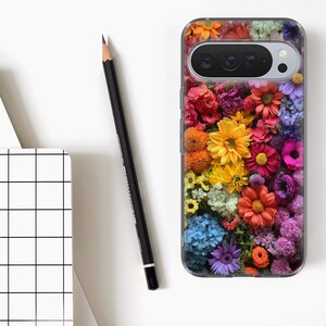 May include: A clear phone case featuring a collage of colourful flowers in shades of red, yellow, orange, and purple. A black pencil and a white notebook with a grid design are also present.