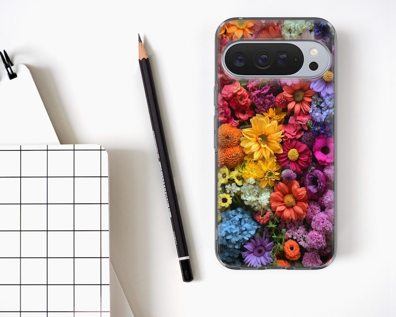 May include: A clear phone case featuring a collage of colourful flowers in shades of red, yellow, orange, and purple. A black pencil and a white notebook with a grid design are also present.