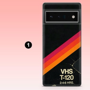 May include: Black phone case with a retro VHS tape design. The case features a diagonal stripe in red, orange, and yellow. The text "VHS T-120" and "2-4-6 HRS." are printed on the case.