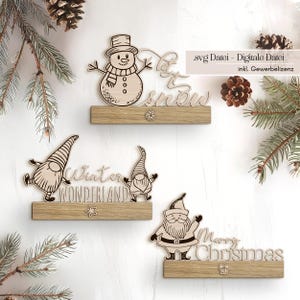 May include: Wooden Christmas decorations featuring a snowman with "Let it Snow", two gnomes with "Winter Wonderland", and Santa Claus with "Merry Christmas". Each decoration is mounted on a wooden base with decorative accents. The image includes text: ".svg Datei - Digitale Datei inkl. Gewerbelizenz".
