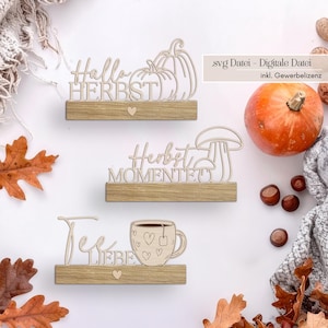 May include: Wooden fall-themed decorations with the phrases "Hallo HERBST", "Herbst MOMENTE", and "Tee LIEBE". Each phrase is on a wooden shelf with a heart. The decorations include pumpkins, a mushroom, and a teacup.