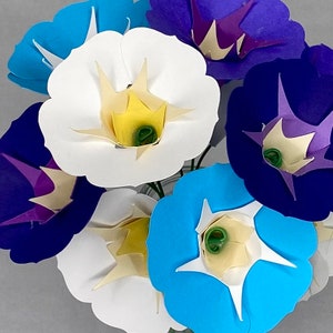 Puede incluir: Un ramo de flores de papel en varios colores, incluyendo azul, morado, blanco y amarillo. Las flores est&aacute;n dispuestas en un jarr&oacute;n y tienen un aspecto delicado y en capas.