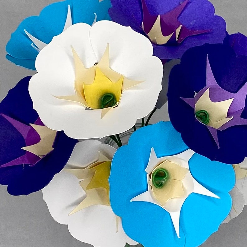 Puede incluir: Un ramo de flores de papel en varios colores, incluyendo azul, morado, blanco y amarillo. Las flores est&aacute;n dispuestas en un jarr&oacute;n y tienen un aspecto delicado y en capas.